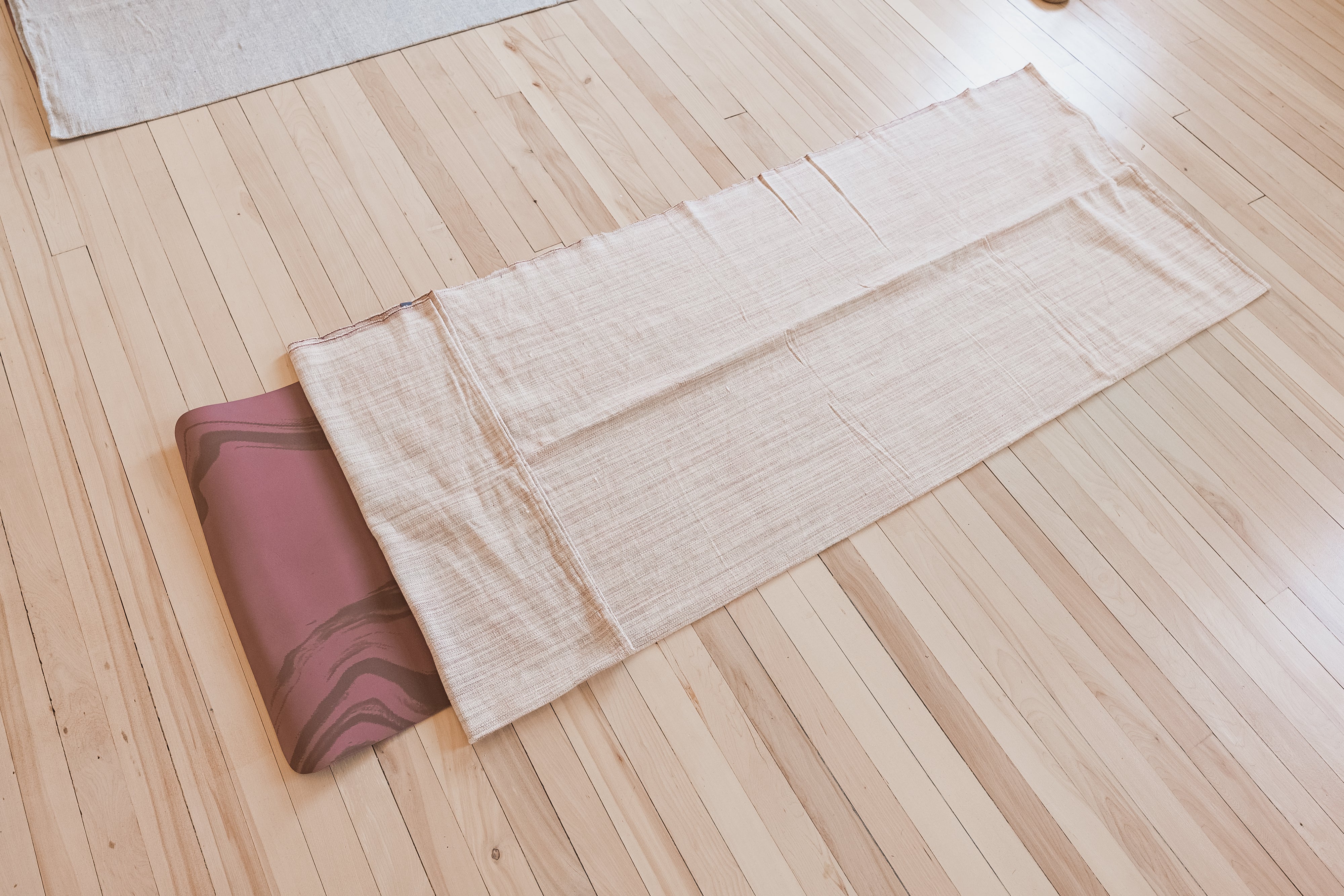 Yoga mat on a wooden floor with a yoga blanket on top of it.