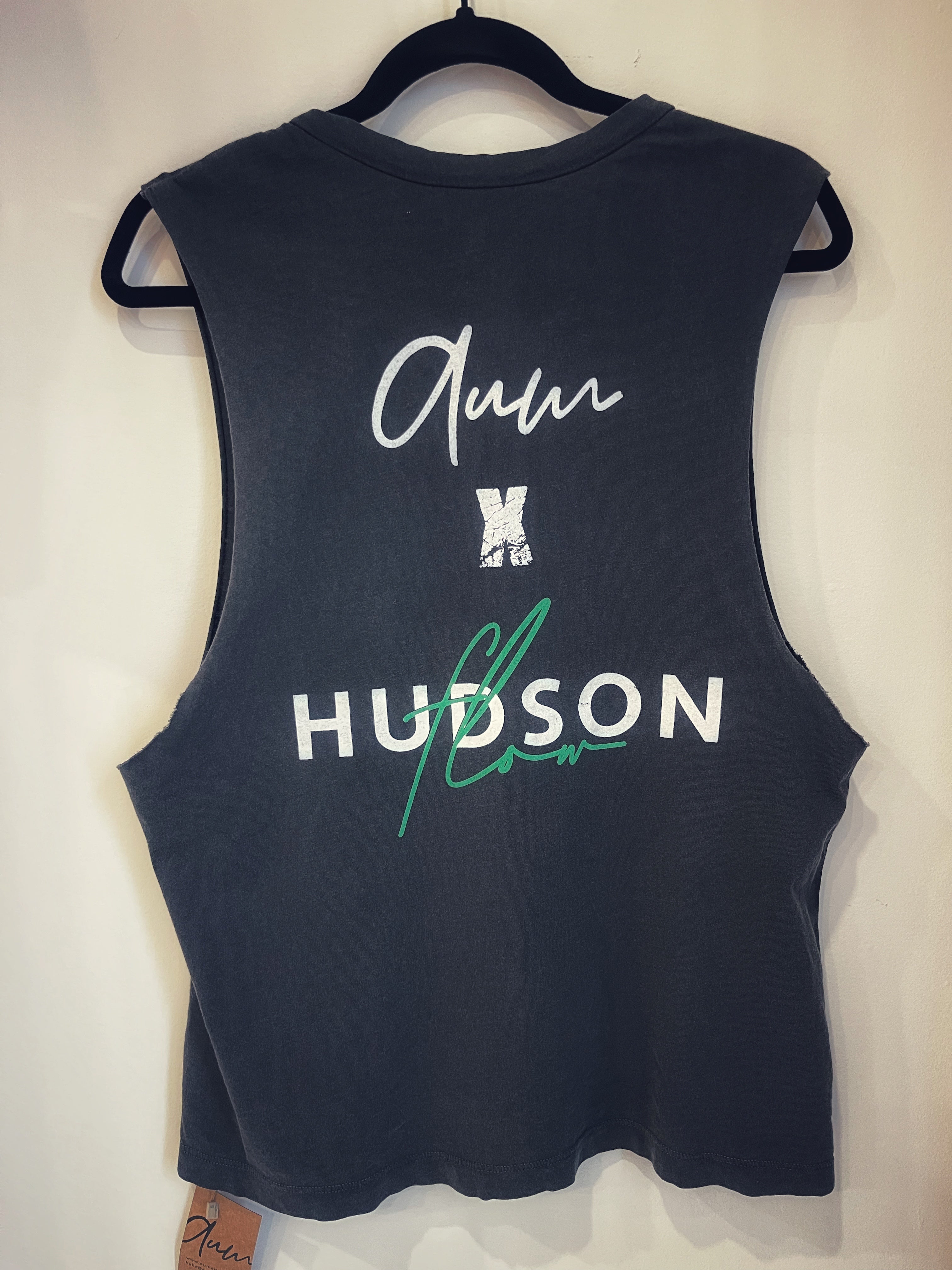 The back of a black tank with the phrase "Aum X Hudson Flow" in white and green across the back.