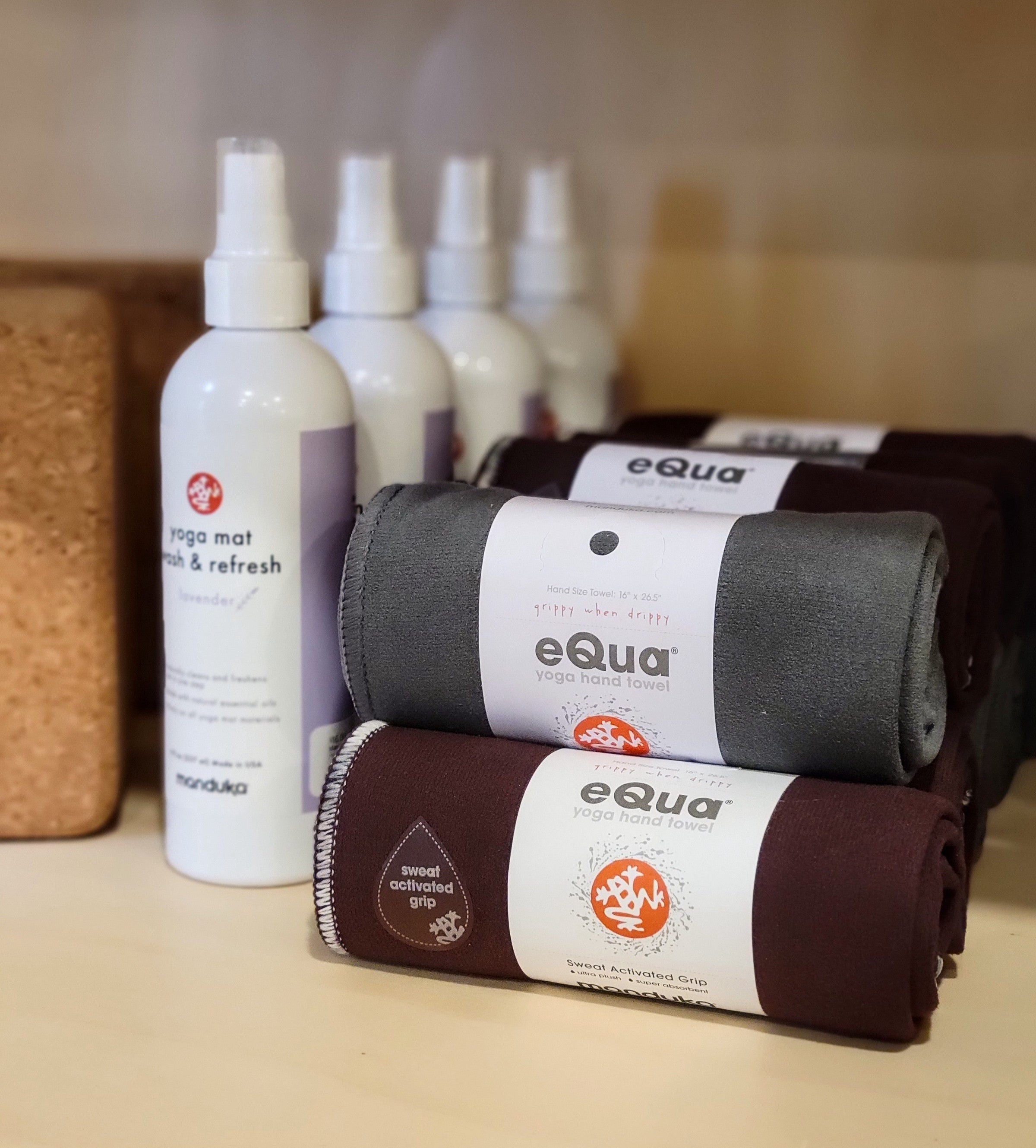 Rolled up yoga towels next to mat spray on a shelf.