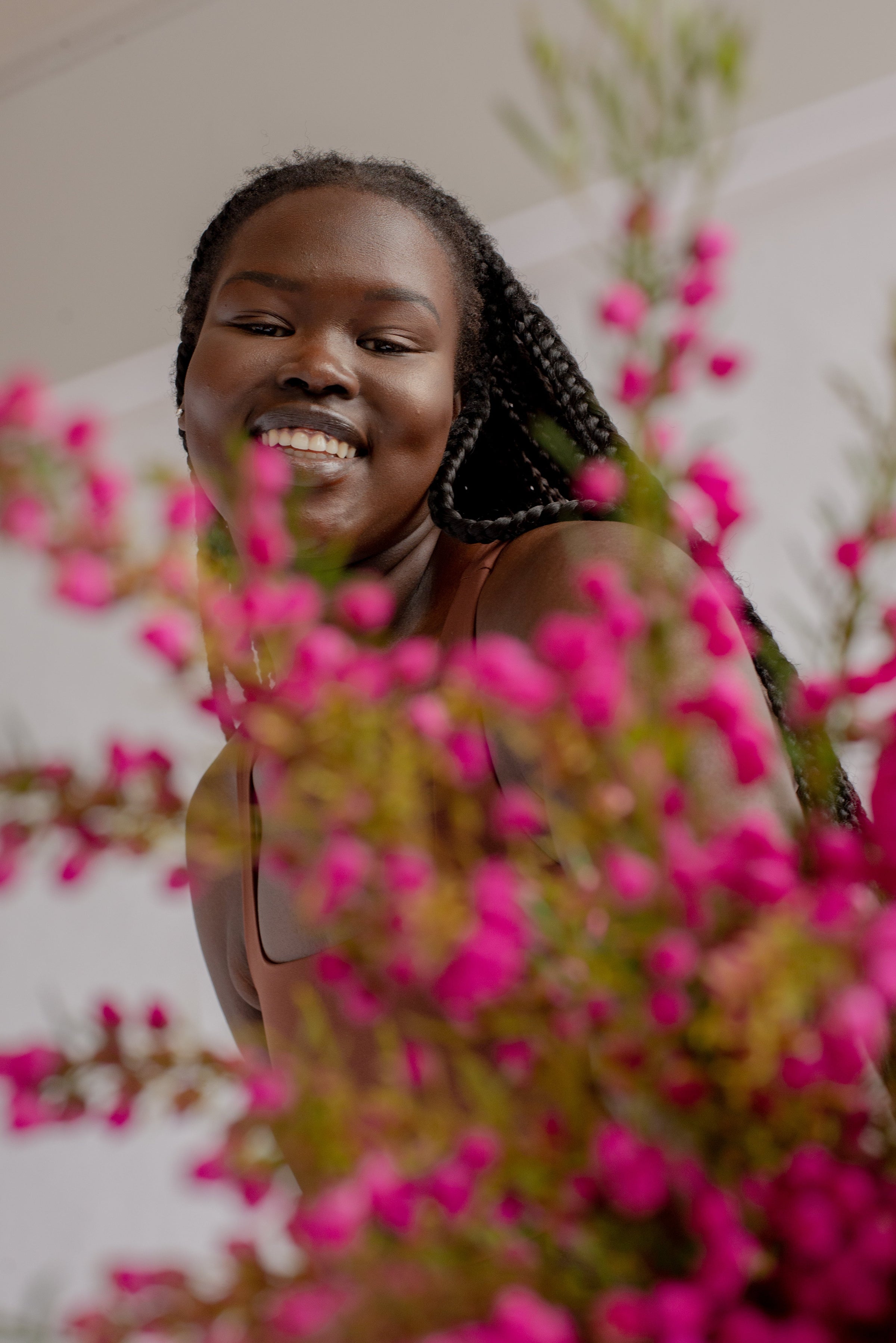 A woman wearing Girlfriend Collective and smiling and holding some pink flowers close to the camera.