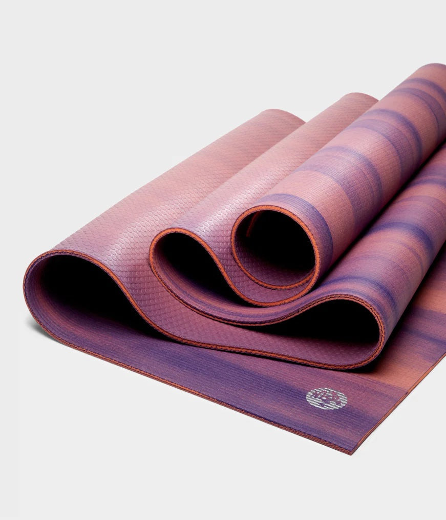A pink and purple yoga mat laying in folds on a white background.