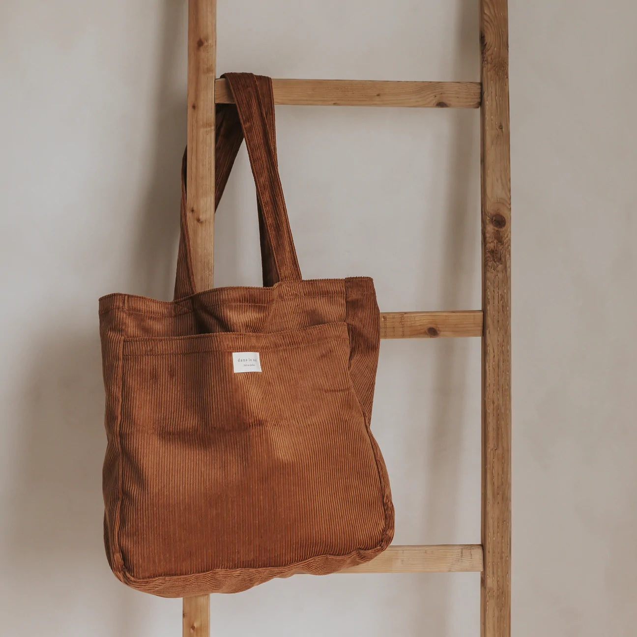 A brown Dans Le Sac tote hanging from a wooden ladder.