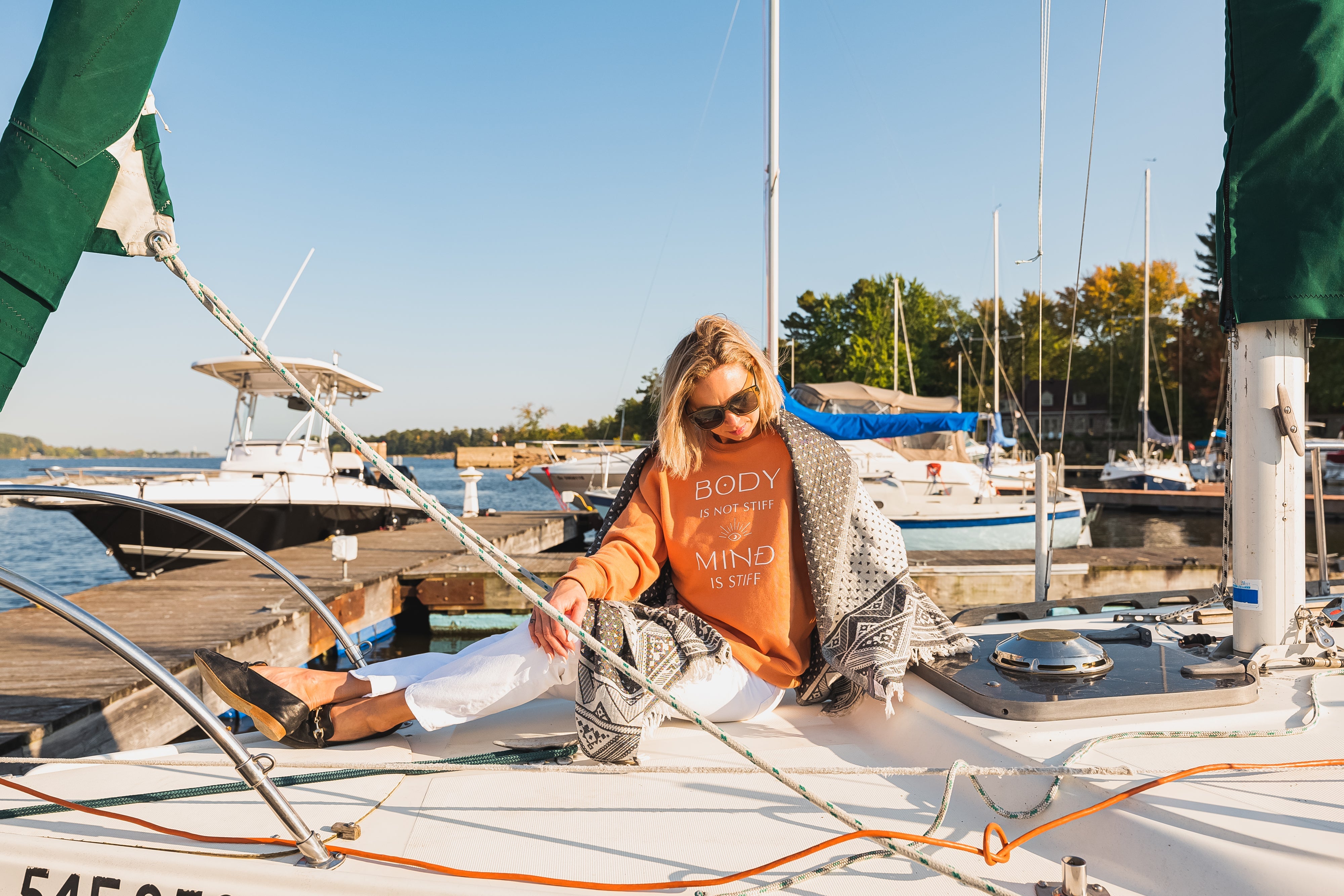 Woman on a sail boat wearing a bright orange sweater, white pants and sunglasses.