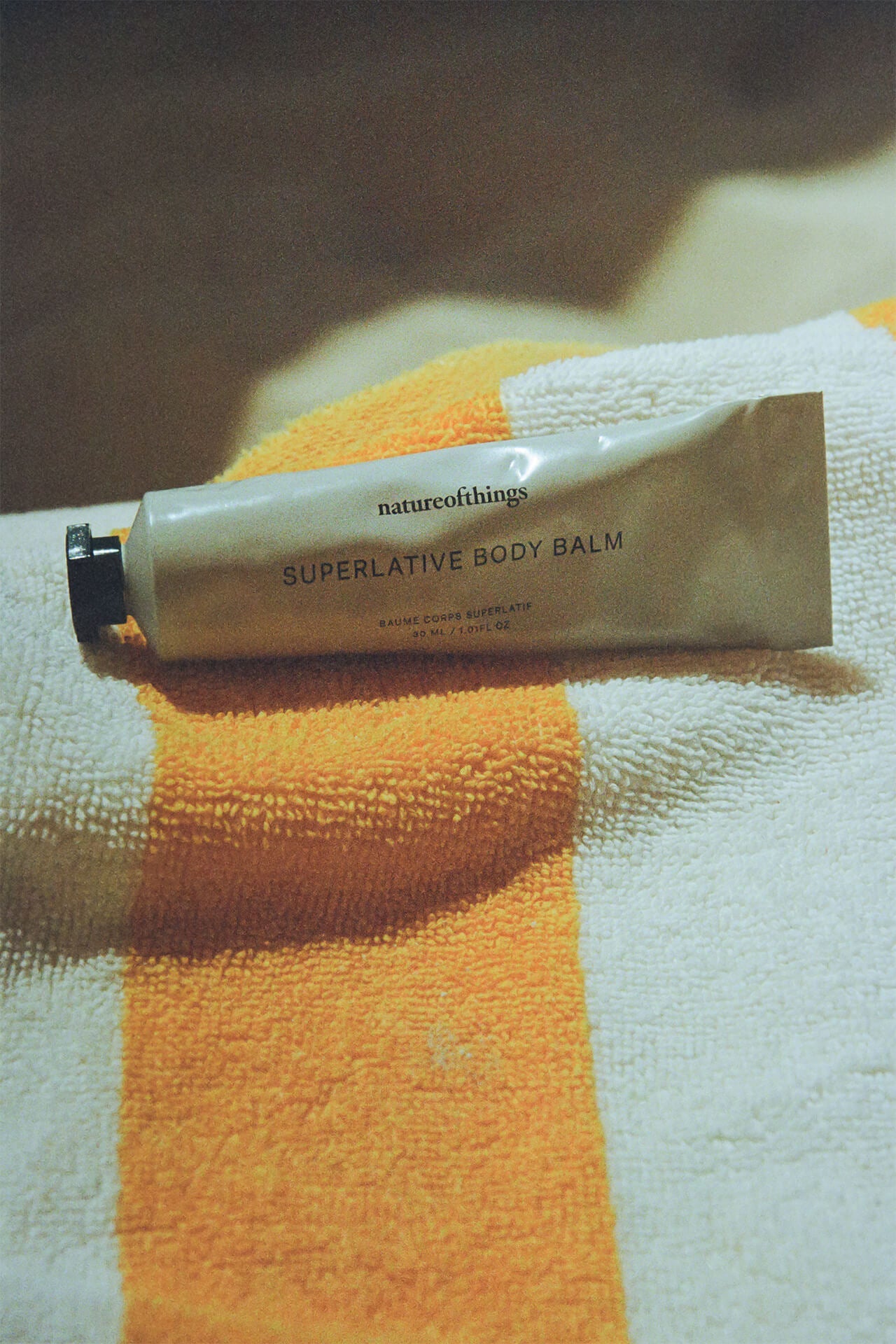 A tube of body balm sitting on a yellow and white towel.