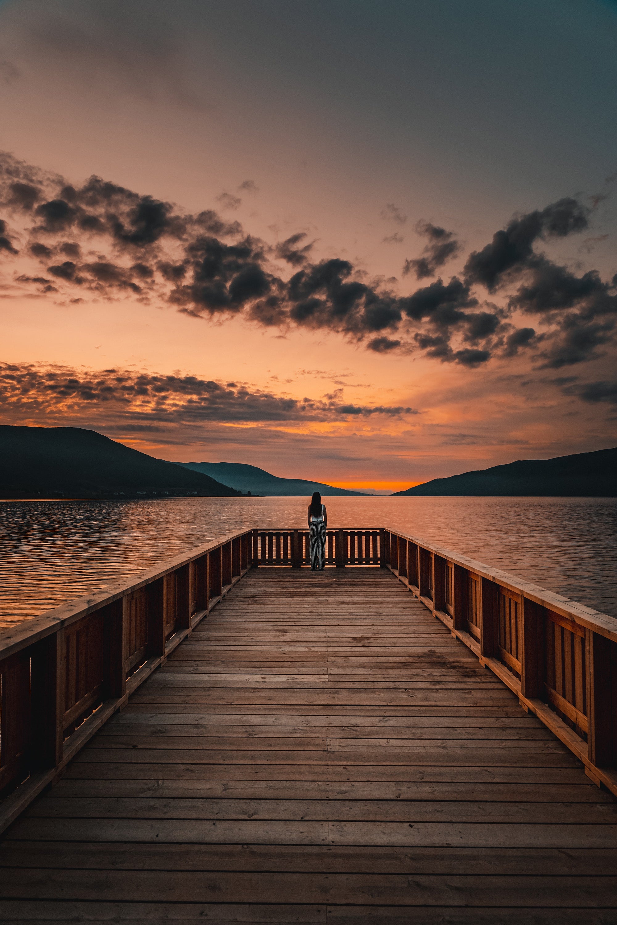 Woman standing at the end of a long dock at sunset.