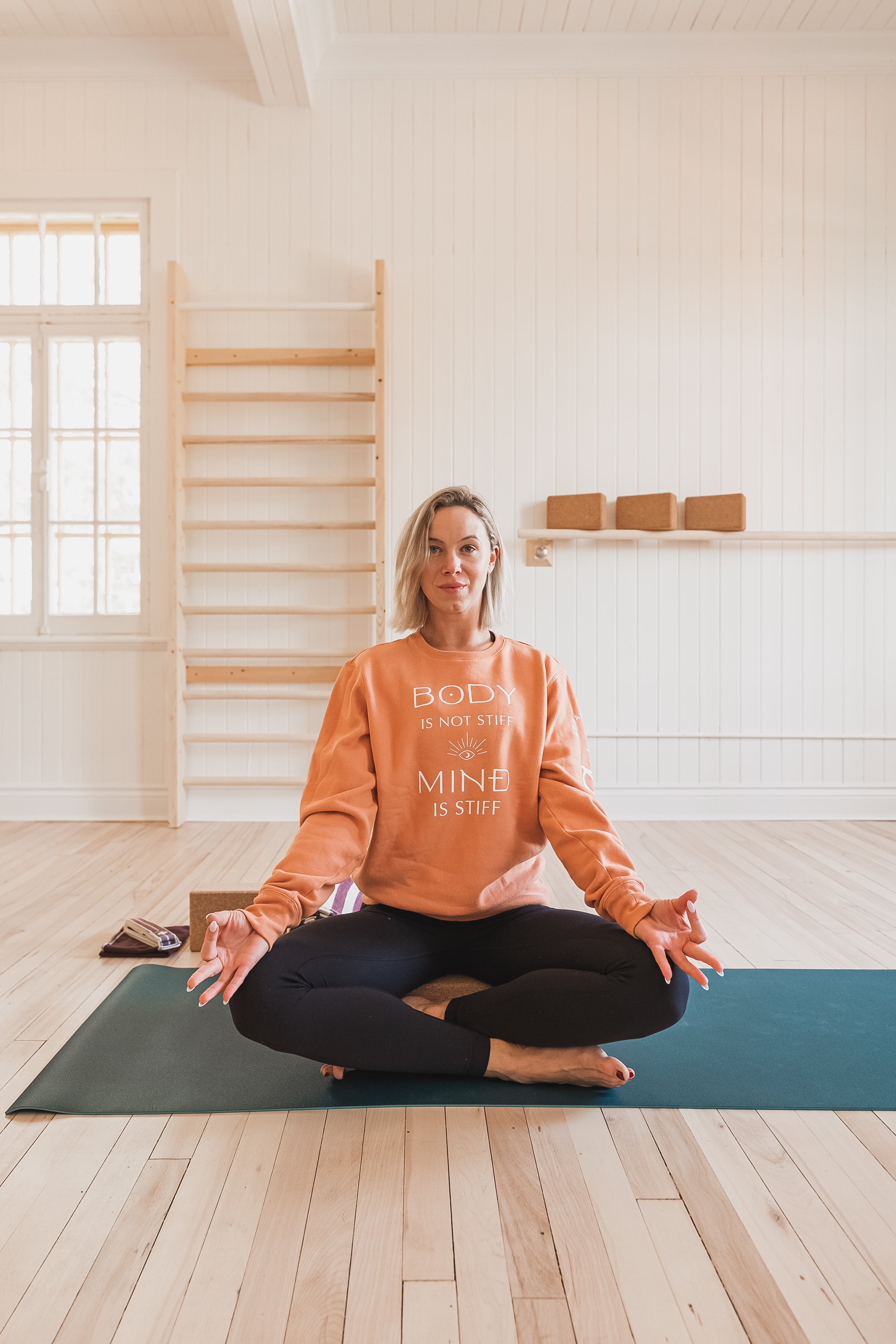 A woman on a yoga mat wearing the AUM Collection Mind is Stiff Crewneck.